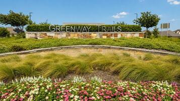 Zona ajardinada con un letrero que dice 'GREENWAY TRAILS' y una variedad de flores.