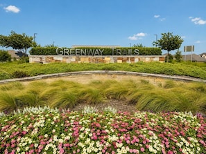 A landscaped area with a sign reading 'GREENWAY TRAILS' and a variety of flowers. - Peaceful Escape | Backyard | Community Pool & Park (Midlothian)