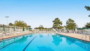 Une piscine d’un bleu éclatant, bordée de chaises longues et d’ombrelles, et entourée d’arbres et d’une clôture.