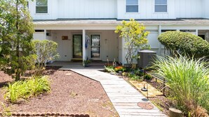 Une maison blanche à deux étages, dotée d’un porche abrité, portant le numéro 253, et d’un jardin bien entretenu avec diverses plantes et un sentier en bois.
