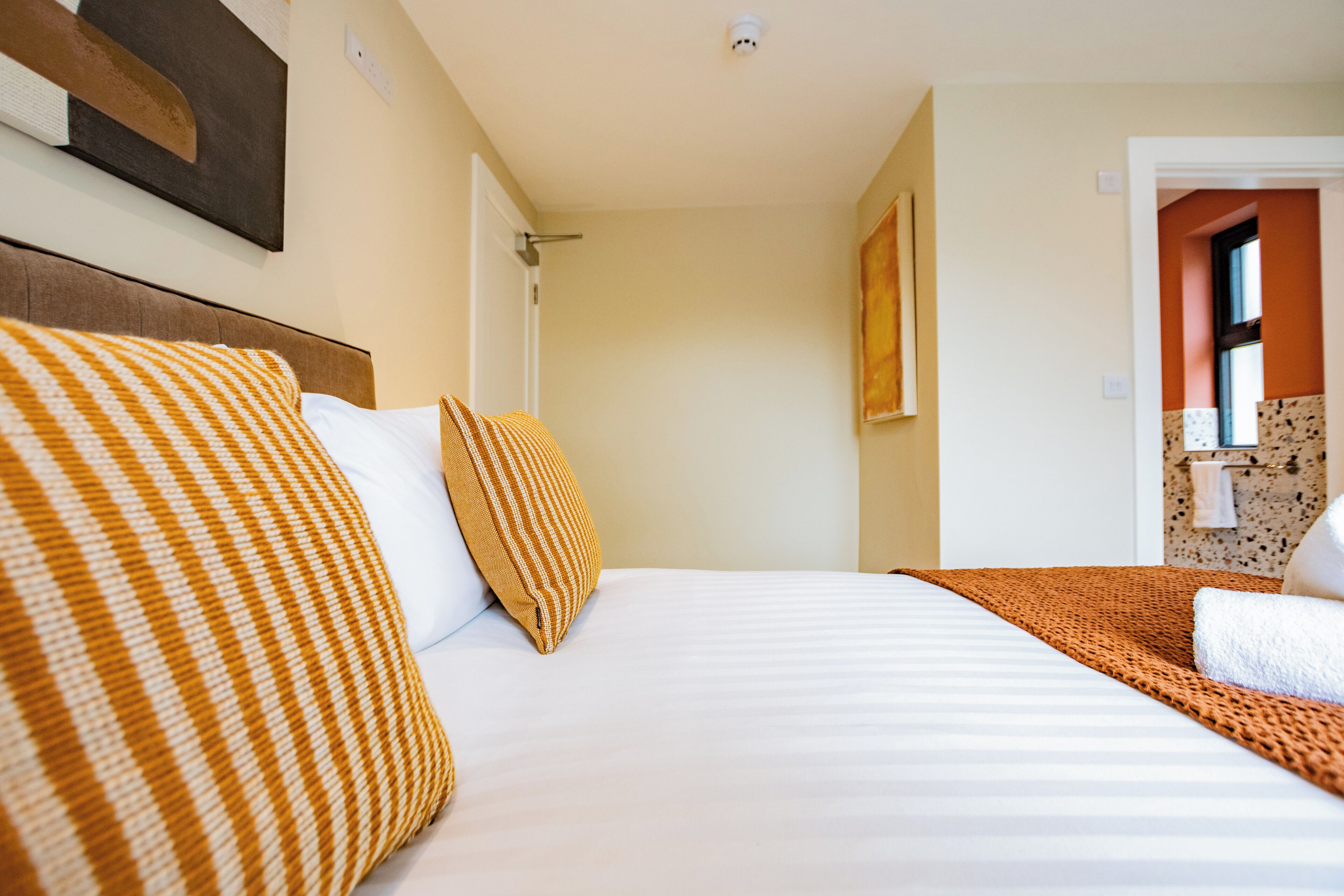 A hotel room with a bed, pillows, a blanket, a wall-mounted artwork, and a bathroom visible through an open door.