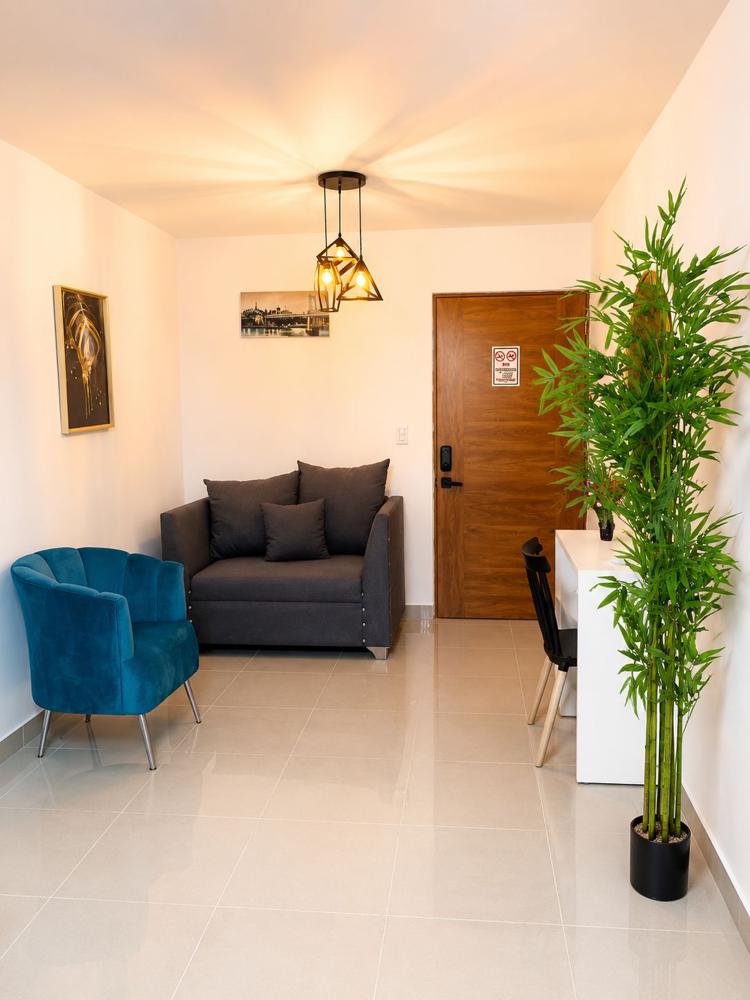 Una sala de estar moderna con un sofá, un sillón azul, una lámpara colgante y una planta de bambú.
