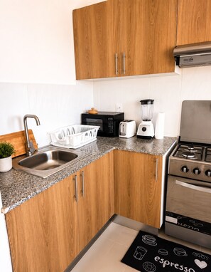 Eine kompakte Küche mit Holzschränken, einer Spüle, einem Herd, einer Mikrowelle, einem Toaster und einem Mixer.