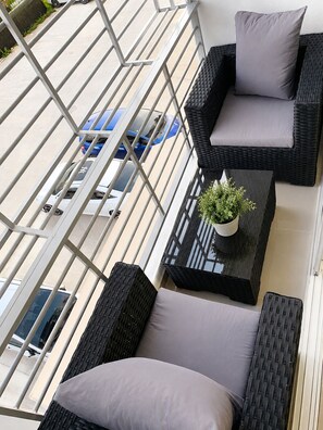Ein Balkon mit Korbmöbeln, einem Tisch mit einer Pflanze und Blick auf geparkte Autos.