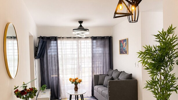 Una sala de estar moderna con un sofá, una mesa de comedor con sillas, un espejo grande y un ventilador de techo.