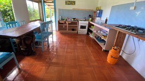 A kitchen with a dining table, chairs, a stove, an oven, and a gas cylinder. - Ocean-View Room (Hanga Roa)