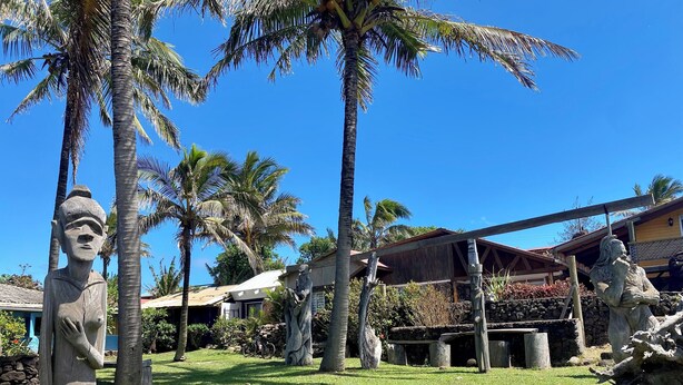 A tropical garden with stone statues, palm trees, and a wooden structure. - Ocean-View Room (Hanga Roa)