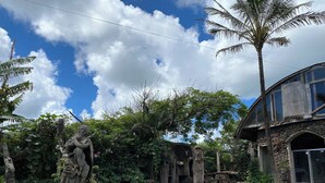 A courtyard with a stone statue, a wooden bench, and a house with a stone facade. - Ocean-View Room (Hanga Roa)