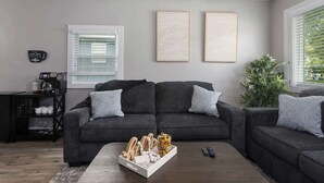 Een moderne woonkamer met een grijze zithoek, een salontafel met decoratieve objecten, en een klein zwart bijzettafeltje met een koffieapparaat.