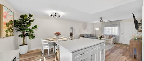 A modern kitchen with white cabinetry, a central island, and a dining area with a table and chairs.