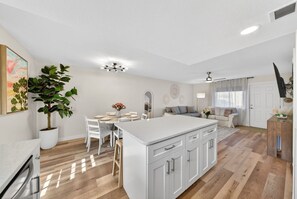 A modern kitchen with white cabinetry, a central island, and a dining area with a table and chairs. - Coastal Townhome in Gated Resort w Patio & Pool (Panama City Beach)