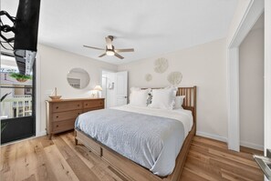 A bedroom with a bed, wooden dresser, ceiling fan, and a view of the outside. - Coastal Townhome in Gated Resort w Patio & Pool (Panama City Beach)