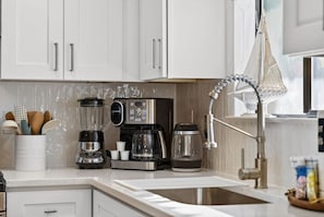A kitchen with white cabinets, a coffee maker, a blender, and a kettle. - Coastal Townhome in Gated Resort w Patio & Pool (Panama City Beach)