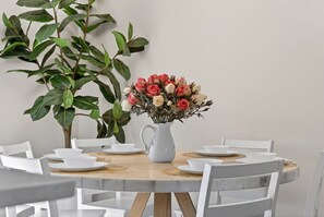 A round dining table with white chairs, a white pitcher with flowers, and a large green plant in the background. - Coastal Townhome in Gated Resort w Patio & Pool (Panama City Beach)