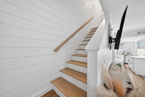A staircase with wooden steps and white walls, leading to a kitchen area with white cabinets and a window. - Coastal Townhome in Gated Resort w Patio & Pool (Panama City Beach)