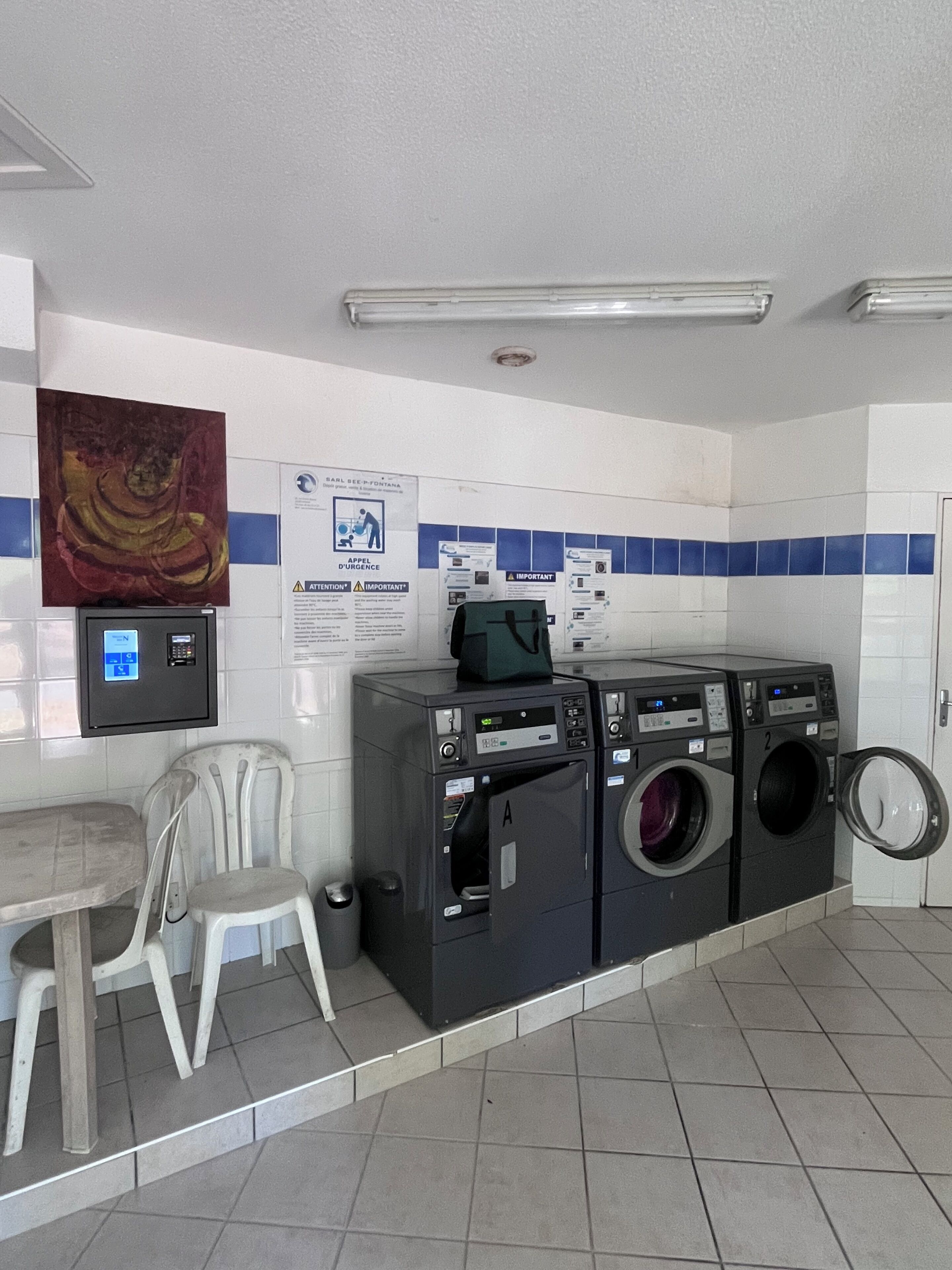 A public laundry facility with multiple washing machines, a chair, and informational posters on the wall.