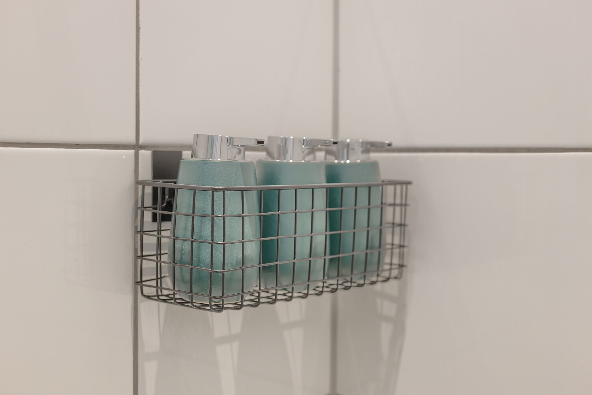 Un panier métallique contenant deux bouteilles, fixé à un mur recouvert de carreaux blancs.