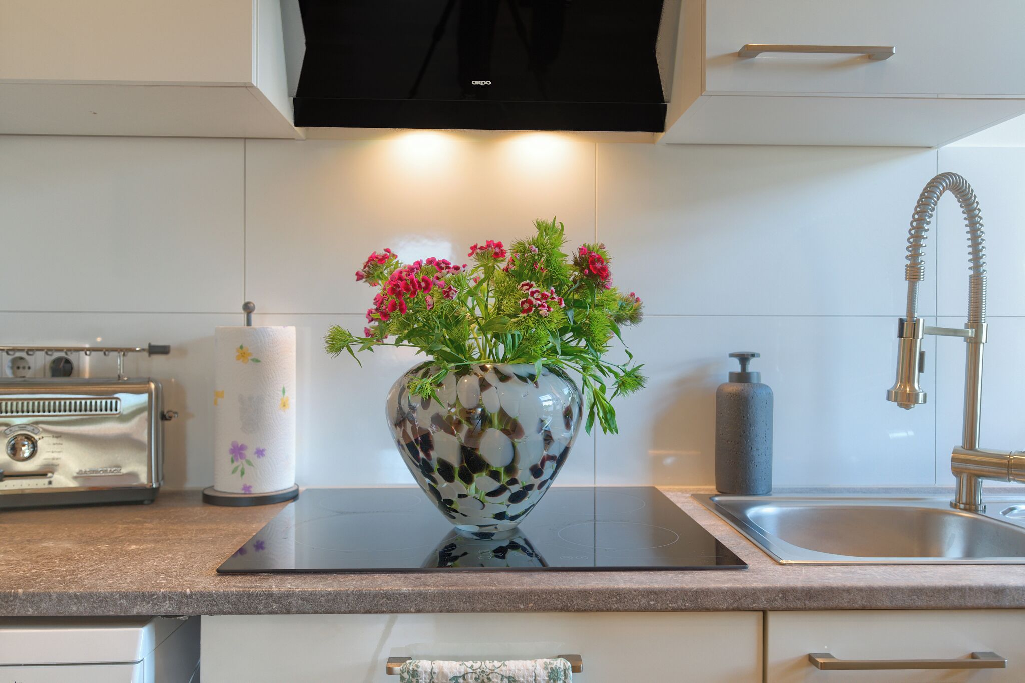 A kitchen with a modern stove, a sink, and a vase with flowers on the counter.