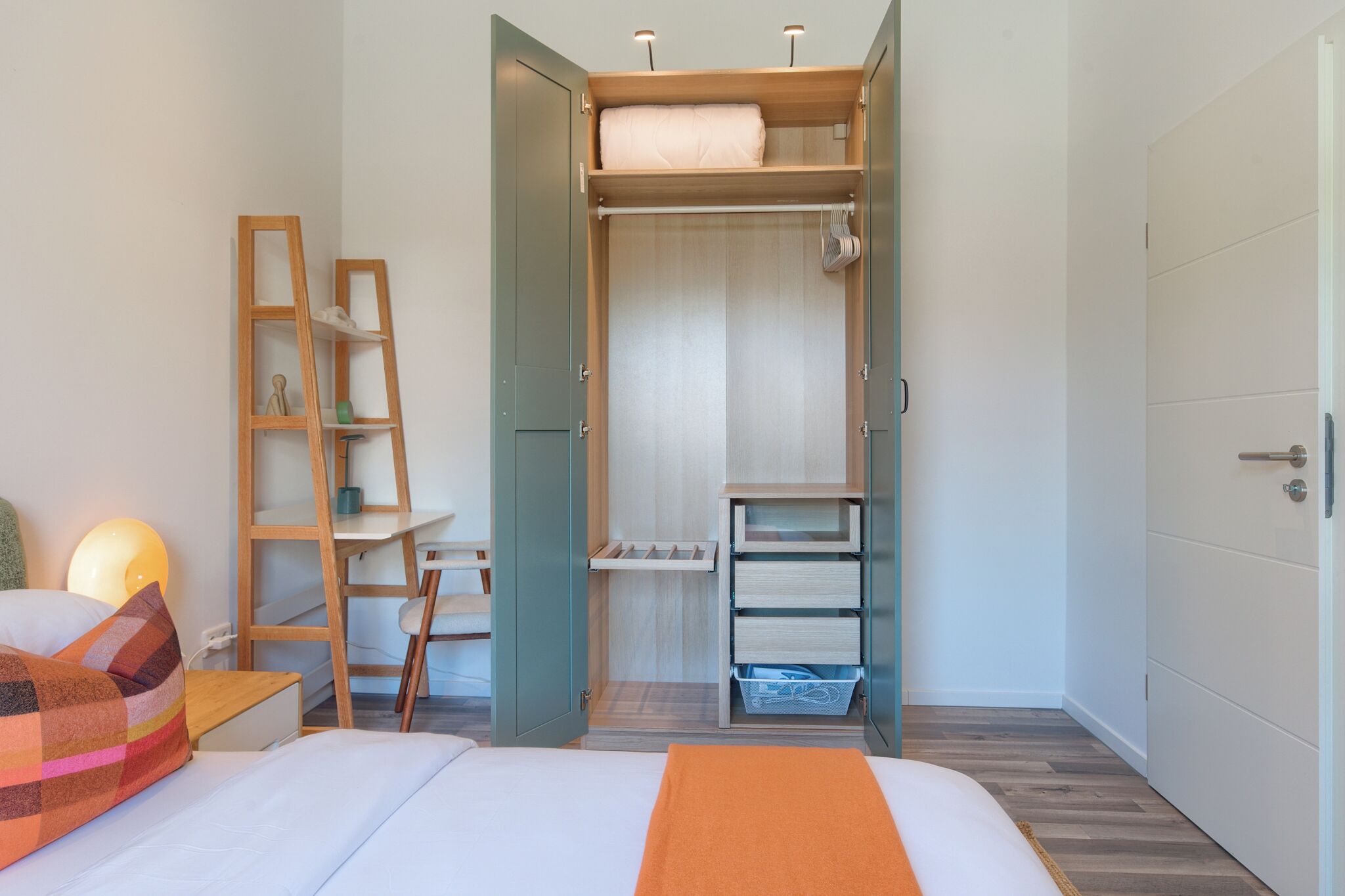 Une chambre à coucher comprenant un lit, un bureau et une armoire ouverte avec des étagères et des tiroirs.