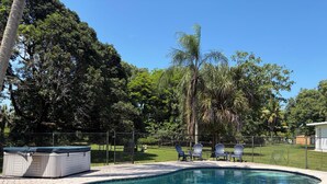 Una piscina con borde de ladrillo, rodeada por una valla, y tres sillas Adirondack.
