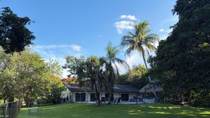 Una casa con patio cercado, una palmera y una construcción con techo de paja.