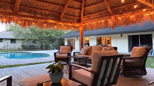 Un patio al aire libre con mobiliario de mimbre, una piscina y un techo de paja.