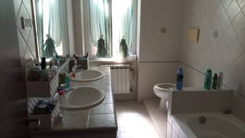 Une salle de bain avec deux lavabos, des toilettes, une baignoire et une fenêtre avec des rideaux.