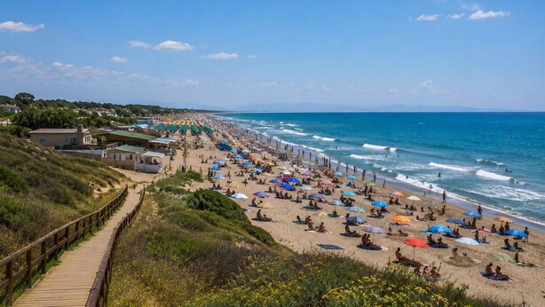 A beach with a wooden boardwalk, beach umbrellas, and people sunbathing.