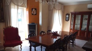 A dining room with a large wooden table, chairs, a red armchair, a fireplace, and a clock on the wall.