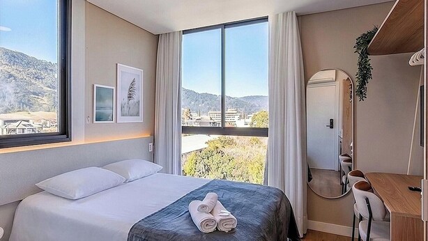 Ein Hotelzimmer mit Bett, Schreibtisch, Spiegel und großen Fenstern mit Blick ins Freie.