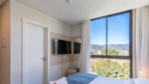 A hotel room with a bed, a TV, a window with a view, and a door. - Modern Apt. W/city View in Urubici Ust0409 (Urubici)