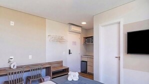 A compact hotel room with a bed, a small seating area, a kitchenette, and a TV. - Modern Apt. W/city View in Urubici Ust0409 (Urubici)