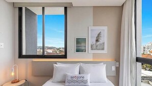 Hotelkamer met een bed, nachtkastje met lamp, raam met uitzicht op gebouwen en een ingelijst schilderij aan de muur.