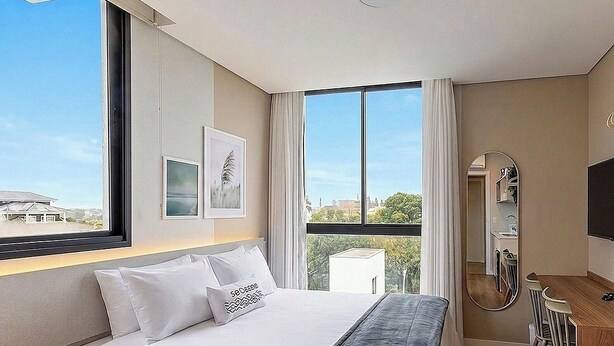 Een moderne hotelkamer met een groot bed, een nachtkastje, een spiegel en een raam met uitzicht over de stad.