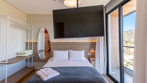 Une chambre d’hôtel équipée d’un lit, d’une télévision, d’un miroir, d’une table de chevet et d’une fenêtre donnant sur un paysage agréable.
