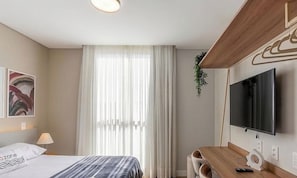 A hotel room with a bed, a desk, a TV, and a window with curtains. - Comfort W/city View in Urubici Ust0506 (Urubici)