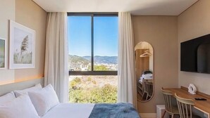 Une chambre d’hôtel comprenant un lit, un bureau, une chaise, une télévision, une fenêtre donnant sur la ville et un porte-manteau.