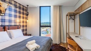 Habitación de hotel con cama, escritorio, televisión, ventana grande y vistas al exterior.