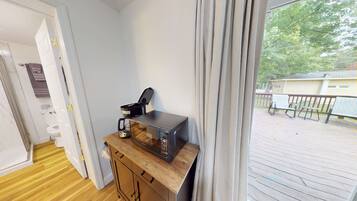 A compact room with a wooden cabinet, a microwave, and a coffee maker. A window with curtains is visible, offering a view of an outdoor deck.
