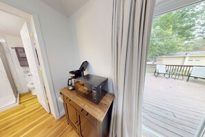 Habitación compacta con un armario de madera, microondas y cafetera. Se ve una ventana con cortinas, que ofrece vistas a una terraza exterior.