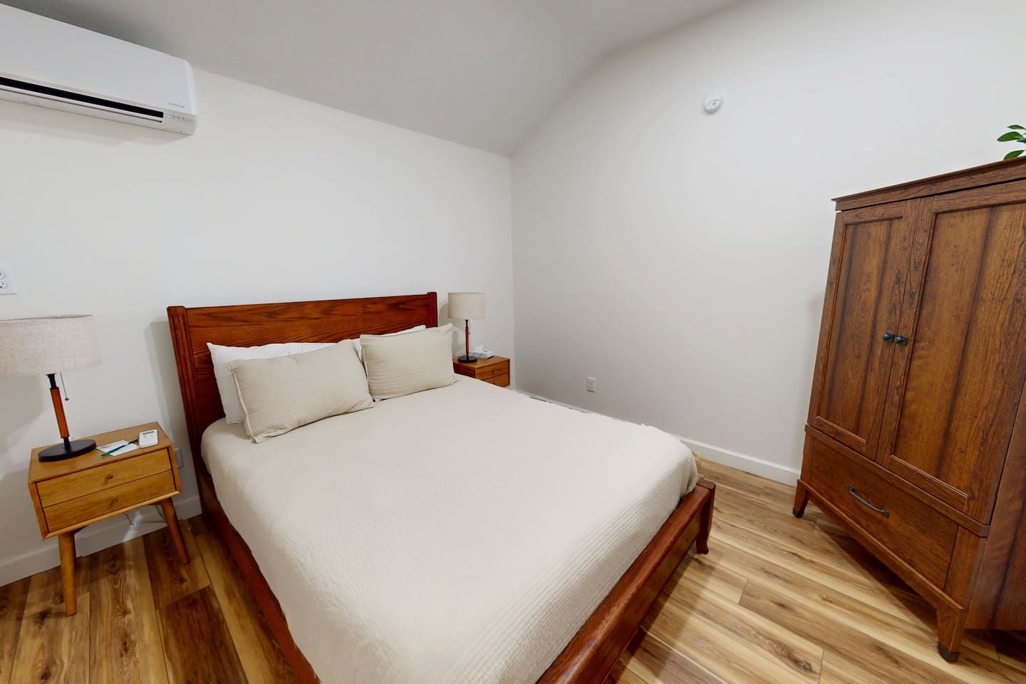 Une chambre à coucher avec un lit en bois, une table de chevet avec une lampe, une armoire et un appareil de climatisation fixé au mur.
