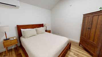 Une chambre à coucher avec un lit en bois, une table de chevet avec une lampe, une armoire et un appareil de climatisation fixé au mur.
