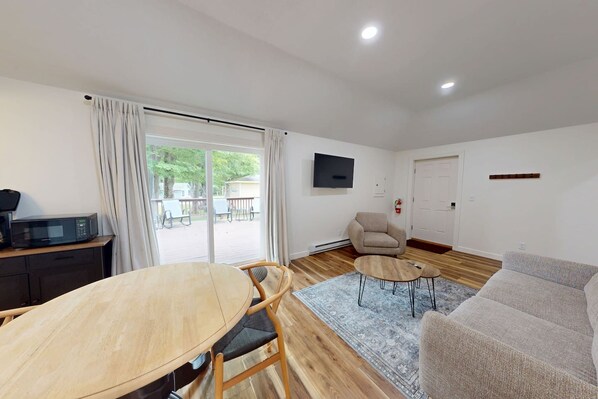 A living room with a dining table, sofa, and a flat-screen TV mounted on the wall.