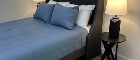 Ein Bett mit dunklem Kopfteil, zwei Nachttischlampen und Holzboden.