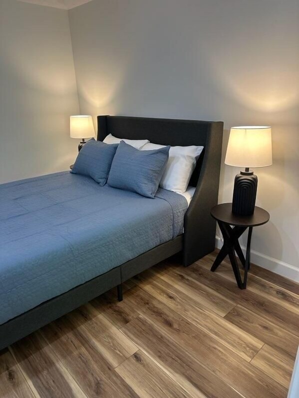 Una cama con cabecera oscura, dos lámparas de noche y suelo de madera.