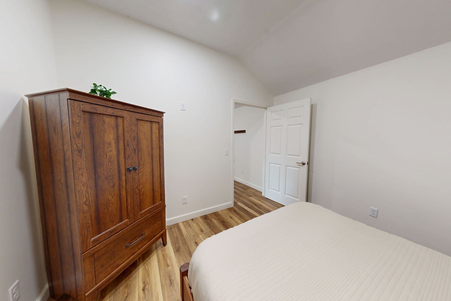 Un dormitori amb un armari de fusta, un llit i una porta que dona a una altra habitació.