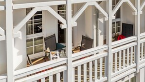 Een meerlaags balkon met witte leuningen, een tafeltje met een lamp en een stoel.