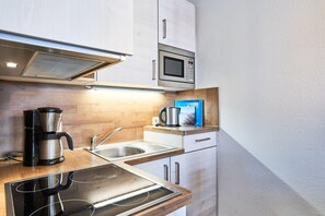 Eine kleine Küche mit integriertem Mikrowellenherd, einer Kaffeemaschine und einem Spülbecken.
