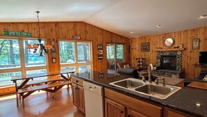 A spacious kitchen with wooden cabinets, a dishwasher, a sink, and a stone fireplace. - Beautiful 3 bed/2bath updated cabin w sandy swimmable frontage & great fishing (Eagle River)