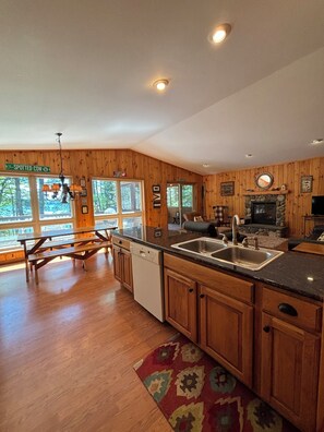 A spacious kitchen with wooden cabinets, a dishwasher, a sink, and a stone fireplace. - Beautiful 3 bed/2bath updated cabin w sandy swimmable frontage & great fishing (Eagle River)